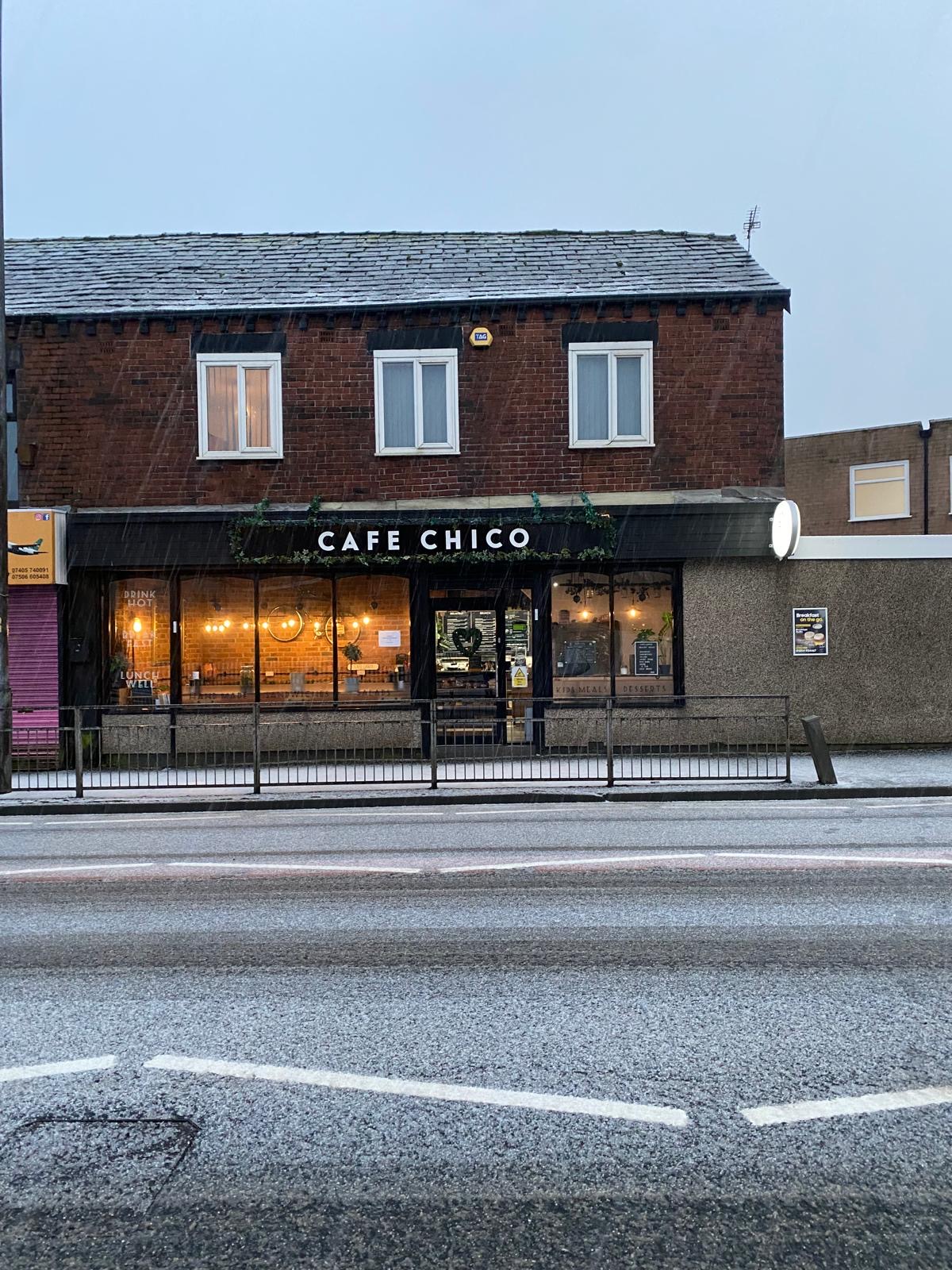 Café Chico on a moody, rain-grey day on St Helens Rd, Bolton — the storefront stands warm and lit behind the weather